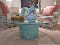 Full view of the modernist cocktail table showing the aqua art glass cylindrical base with ice brick pattern and matching round beveled glass top with aqua tint, decorated with several objects on top.