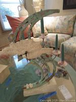 Photo showing the sculptural verdigris clock with curved metal and copper/stone resin base, paired with metal candle sticks on glass table.