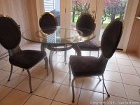 Round glass-top table and four chairs arranged on tiled floor near doors
