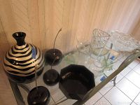 Top-down view of tableware and decorative pieces including black and white striped vase, black decorative apples, black geometric bowl and clear glass bowls.