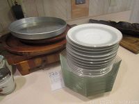 Stack of white decorative plates and clear square glass bowls topped with a large aluminum baking pan on wooden boards.