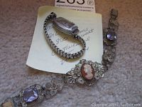 Image showing the antique silver filigree cameo amethyst bracelet placed beside the vintage ladies watch on a fabric surface with a note underneath.