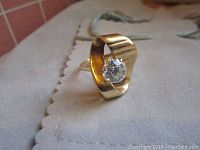 Angled view of ring showing wide gold band and solitaire diamond.