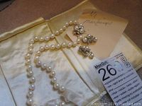 Full view of pearl necklace draped and two earrings on satin background with lot tag