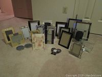 Various picture frames arranged on carpet showing diversity in size, style, and color including wood, metal, and glass frames.