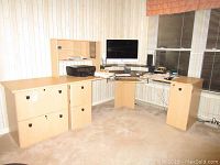 L-shaped computer desk with a small hutch, cabinets and drawers. Desk has light wood finish. Contents like computer monitor, keyboard, printer seen but not included.