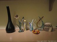 Wide shot of all decorative items including tall black vase, brass flower display, three art glass pieces, glass heart, and two shell boxes.