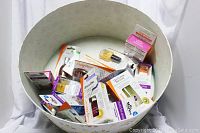 Top view of a white round hat box filled with assorted new Sally Hansen nail care products in original packaging.