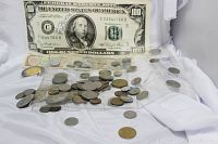 View showing a large fake $100 bill behind assorted foreign coins and paper currency spread out on white fabric.