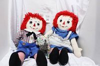 Front view showing both Raggedy Ann and Andy dolls sitting side by side with visible facial features, outfits, and condition.