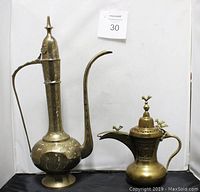 Photo showing both brass teapot decanters side by side, highlighting size difference and overall shape.