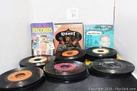 Box filled with stacks of 45 RPM records and Official Price Guide to Records displayed upright in background, showing variety of records with some covers visible.