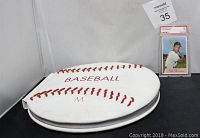 A white baseball-shaped padded book with red stitching and the word 'BASEBALL' on it, next to the authenticated and encased 1954 Cal Abrams baseball card.