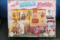 Front view of the Bratz World Mansion box showing artwork of the dollhouse and Bratz dolls, highlighting features such as dance floor lighting, spiral staircase, opening doors, and juice bar.
