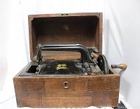 View of antique Grover & Baker sewing machine inside wooden box with lid open showing hand-crank and metal work.