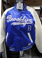 Front view of the blue and white satin bomber jacket with rhinestone "Brooklyn" embroidery shown hanging on a hanger with maxsold tag visible.