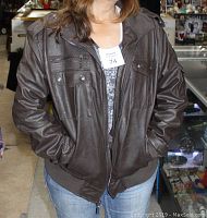 Photo of front view of the brown faux leather bomber jacket worn by model showing zipper closure, flap pockets with buttons, and epaulettes on shoulders.