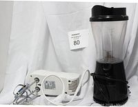 Photo showing two kitchen appliances: a black Maxi-Matic blender with clear container and a white Hamilton Beach hand held mixer with beaters, laid on side