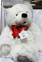 Front view of the large white teddy bear sitting upright, showing full body and red bow with heart detail.