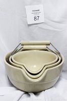 Three nested beige porcelain mixing bowls with metal handles and beige wooden grips, showing the pour spouts and textured design on the lower half of each bowl