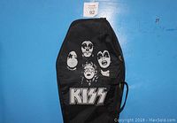 Photo of front of black coffin-shaped guitar case showing printed faces of KISS band members and large KISS logo with hand strap attached.