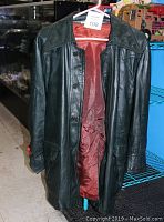 Front view of vintage green leather coat hanging, showing red interior lining and button front closure.