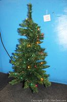 Full view of the artificial Christmas tree showing height and overall tree shape with lit multi-colored lights.