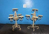 Pair of matching vintage metal candelabras with 4 side arms and center arm, curling legs, cream color against blue background.