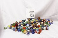 Pile of assorted vintage glass marbles in multiple colors and sizes on white cloth background with auction lot card