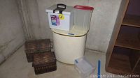Plastic storage bins including a white file cabinet-style bin with black handle, a large white clothes hamper, and clear cereal holder bin with red lid.
