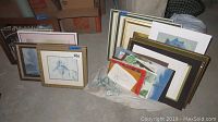 Full view of assorted framed and unframed artwork laid on floor, showing variety of frames and prints