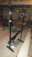 Metal garment rack upright, showing horizontal bars, base shelf, and disassembled parts stacked at bottom. Background shows basement setting.
