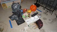 Photo showing all lot items including female bust statue, orange pumpkin decor, black and red fan, trays with cups, various bowls and dishes, crystal flower, and photo album arranged on the floor.