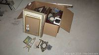Box containing various metal framed pictures of different sizes including large 11x14 frames and smaller ornate vintage frames.