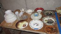 Full table showing an assortment of vintage plates, bowls, tea cups, saucers, and decorative ceramic items with various colors and patterns.