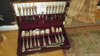 Set of silverplated flatware arranged in red velvet-lined section of wooden case, showing various spoons, forks, and knives.