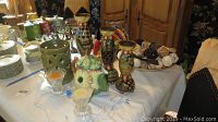 Table displaying three ceramic candle sticks with painted decor, ceramic turkey, teapot, metal bowl with pinecones, glass candle sticks, and ceramic vase