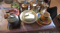Overview of three ceramic fruit canisters with lids and bird handles, ceramic fruit bowls including one with lid, yellow handled vase, and three metal canisters on a rack