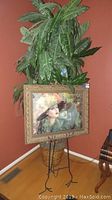 Faux tree plant in basket with painted portrait in gold carved frame on metal easel