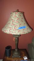 Table lamp with ornate metal base and fabric shade featuring red and green leaf pattern on beige