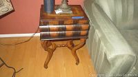 Wooden side table with faux book design and part of adjacent couch, visible chips on legs and corners, showing overall condition