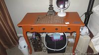 Front angle view of orange painted vanity table showing three drawers, table top showing some wear and chips, metal round drawer pulls.