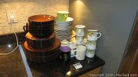 Overview of stacked brown ceramic plates and bowls, and assorted coffee mugs grouped on counter