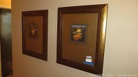 Photo showing two framed Tuscan theme prints on a wall, both with brown and gold wide wooden frames and beige matting inside.