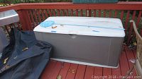 Rubbermaid outdoor deck storage box on wood deck with pool skimmer net on top.