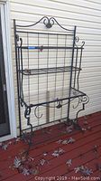 Full view of black metal baker's rack with Plexiglass-topped shelf, showing leaf and vine design
