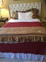 Bed made with floral patterned pillow shams, white pillowcases, deep red blanket, ruffled comforter, and dust ruffle visible.