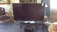 Samsung LED TV on stand in living room, screen off, with papers on stand