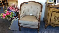 Front view of beige upholstered armchair with button-tufted back and carved wood frame