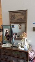 Photo showing the wall mirror with Asian design and raised painted panel, Belleek vase, Lenox candlestick, serving platter, and Asian art figurine on a wooden dresser.